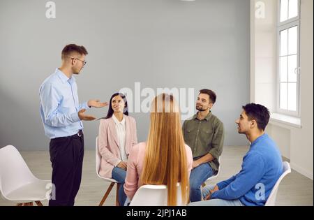 Young smart male coach or team leader speaks during work meeting or creative brainstorm. Stock Photo