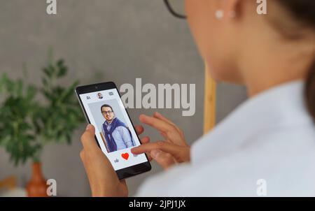 Woman using dating app on mobile phone and swiping user photos and pressing red button. Stock Photo