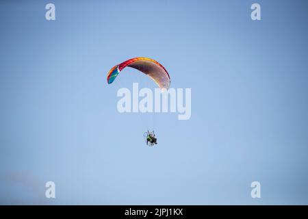 A solo flier enjoying a paramotor flight with multicoloured canopy on a bright early morning summer's day over the Great Orme in Llandudno, N. Wales Stock Photo