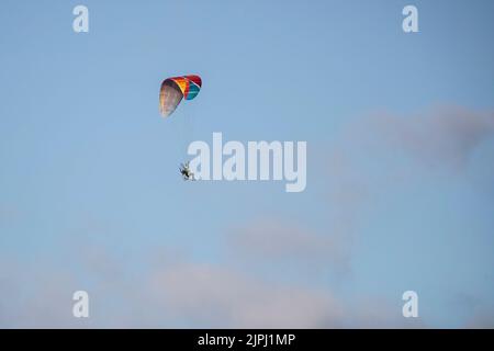 A solo flier enjoying a paramotor flight with multicoloured canopy on a bright early morning summer's day over the Great Orme in Llandudno, N. Wales Stock Photo