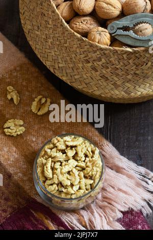 Whole walnuts and a nutcracker in a basket, nut kernels in a jar on a wooden table. Stock Photo