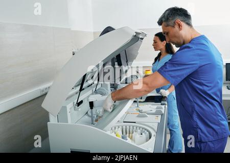 Laboratory technicians analyze blood samples near biochemical automatic ...