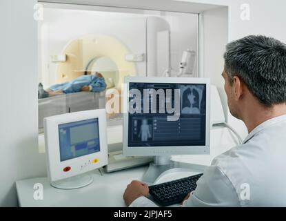 doctor radiologist running CT scan for patient's body lungs from control room. Computed Tomography Stock Photo