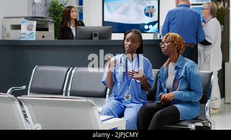 African american nurse and patient using medical hologram to analyze AI holographic metaverse projection in waiting room. People looking at artificial intelligence augmented reality. Tripod shot. Stock Photo