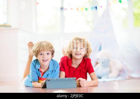 Kids room with teepee tent. Children play computer game on tablet device in white sunny bedroom. Cozy light interior for kid nursery or playroom. Stock Photo