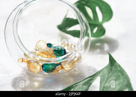 Serum capsules for healthy skin. Blurred background, glass jar with the capsules and exotic monstera leaves. Stock Photo