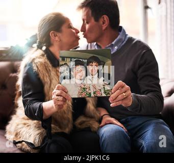 I loved you then, I love you now and forever. a happy mature couple holding up an old photograph of their wedding at home. Stock Photo