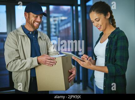 No need for paper when an electronic signature will do. a young woman using a digital tablet to sign for a package from a delivery man. Stock Photo