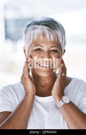 She looks great for her age. Portrait of a cheerful mature woman holding her face with her hands while looking at the camera. Stock Photo