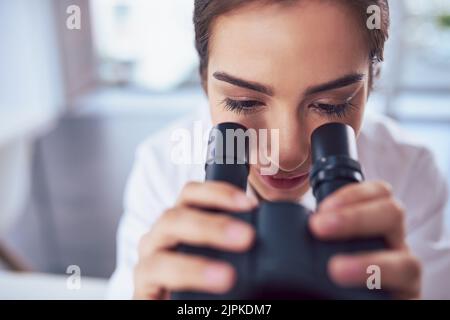 Looking through the lens into another world. Closeup of a focused young female scientist looking through the lens of a microscope inside of a Stock Photo