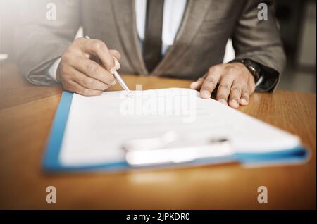 Making changes in the company. an unrecognizable businessperson signing papers inside of the office during the day. Stock Photo