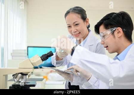 A talented young Asian male medical specialist or scientist working in the lab with senior female supervisor. Stock Photo