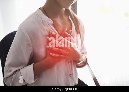 Stress is a high factor in causing chest pain. Closeup shot of an unidentifiable businesswoman holding her chest in pain. Stock Photo