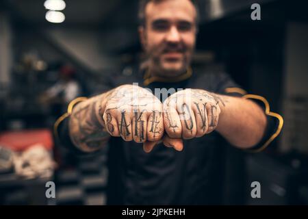 I love baking. a cheerful young chef holding up his fists to the camera with the words tattooed on them Bake Love. Stock Photo