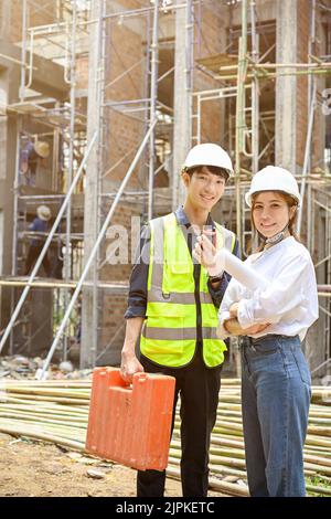 Portrait of a handsome and professional young Asian male civil engineer and beautiful Asian female architect in the construction site. Stock Photo