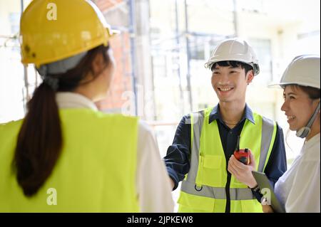 Happy and cheerful young Asian male civil engineer having a great conversation with his construction inspector and architect in the construction site. Stock Photo