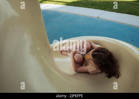 Young girl going down twist slide at park Stock Photo