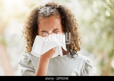 Sick little girl with a flu, blowing her nose and looking uncomfortable. Child suffering with sinus, allergies or covid symptoms and feeling unwell Stock Photo