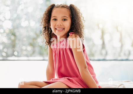 Happy child, cute curls and girl with adorable, sweet and happy smile relaxing at home. Portrait of comfortable, fun and young kid growing with Stock Photo