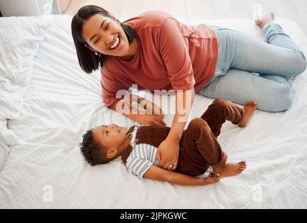 Mother playing, bonding and laughing with her son playful, fun and funny moments together on the bed at home. Parenting and enjoying quality, happy Stock Photo