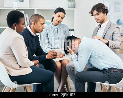 Depression, support and unity by colleagues comforting male after getting bad news at work. Community care from workers sitting together, supporting Stock Photo