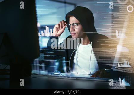 Hes got his eyes on your data. a young hacker cracking a computer code in the dark. Stock Photo