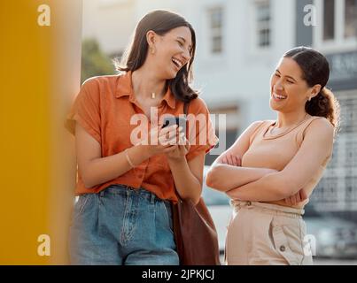 Happy women, friends talking, having fun and laughing while reading a text on a phone together outside. Young, carefree and relaxed females chatting Stock Photo
