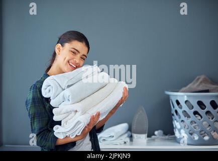 Thats my towels all nice and clean. Cropped portrait of an attractive young woman carrying a pile of towels while doing laundry at home. Stock Photo