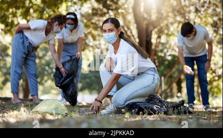 Covid, volunteer and charity with a young woman doing community service and cleaning up the environment with people in the background. Portrait of an Stock Photo