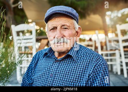 His mind is full of stories. Portrait of a cheerful senior man wearing a hat and standing outside while looking at the camera. Stock Photo