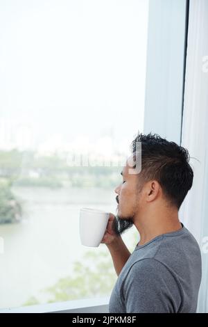 Man drinking aromatic coffee and enjoying the view from his window Stock Photo