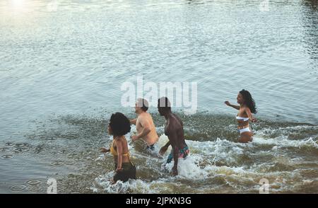 Swimming, fun and freedom in the sea with a group of young friends taking a swim in the ocean by the beach while on holiday or vacation. Diverse Stock Photo