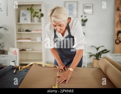 Fashion designer, tailor and seamstress measuring, preparing and making pattern for stylish, trendy and fashionable clothes. Mature woman in workshop Stock Photo