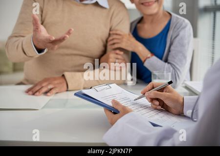 Doctor taking notes when talking to senior couple Stock Photo