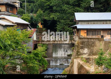 Small waterfall in river through village in Japanese countryside Stock Photo