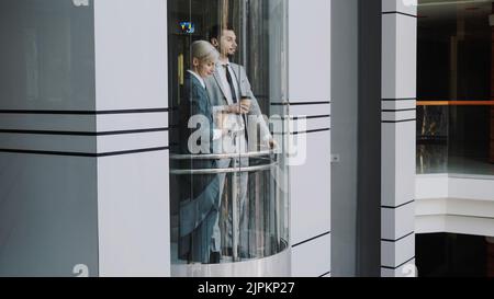 businesswoman and businessman colleagues talking in moving elevator in modern business center indoors Stock Photo