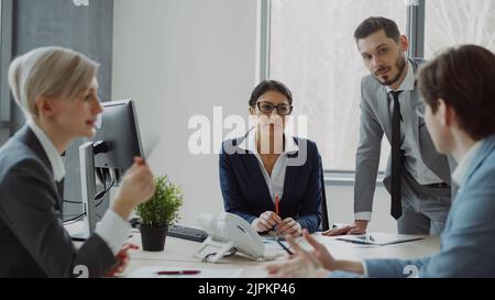 Businesswoman talking with male and female colleagues sitting at the table in modern office indoors Stock Photo