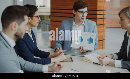 Angry businessman disappointed with company financial reports and scolding employees sitting at the table in meeting room indoors Stock Photo