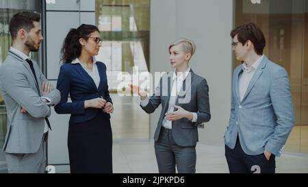 Businesswoman talking to her colleagues while standing in office lobby indoors. Group of business people discussing future deal Stock Photo
