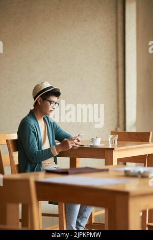 Stylish Asian young man sitting at cafe table and reading text messages Stock Photo