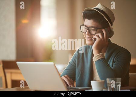Smiling freelancer calling on phone when checking e-mails in his laptop Stock Photo
