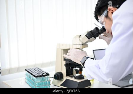 Talented and handsome young Asian male scientist or chemist looking under the Microscope, checking the samples on a microscope slide, working in the l Stock Photo