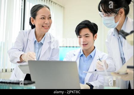 A happy Asian scientist team is working together in the lab, discussing and sharing a new ideas on their medical research. Stock Photo