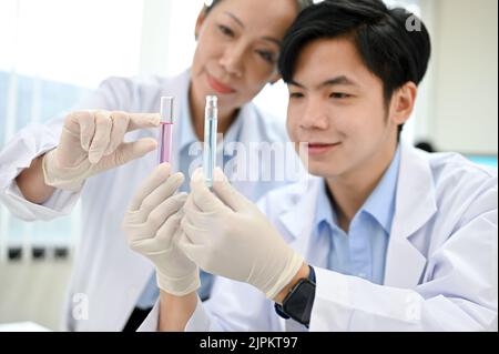 Happy and cheerful young Asian male scientist and senior female supervisor looking at the test tubes together. Pharmaceutical concept Stock Photo