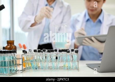 Test tubes with chemical liquid on the table over blurred two scientist working together in the background. close-up image Stock Photo