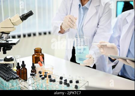 Two expert female scientist in white gown working and testing a new chemical sample together in the laboratory. cropped and close-up image Stock Photo