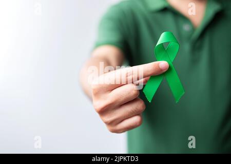 Hand holding green Ribbon for Liver, Gallbladders, bile duct, cervical, kidney Cancer and Lymphoma Awareness month. Healthcare and world cancer day co Stock Photo