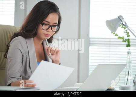 Pensive Asian business lady checking important document Stock Photo