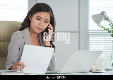 Pensive business woman talking on phone when reading document Stock Photo