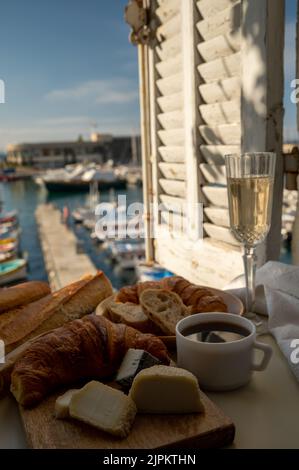 French breakfast with fresh baked croissants, baquett bread, crottin goat cheese, black coffee and view on fisherman's boats in harbour of Cassis, Pro Stock Photo